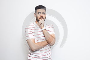 Portrait of thoughtful handsome bearded young man in striped t-shirt standing, looking away and thinking what to do