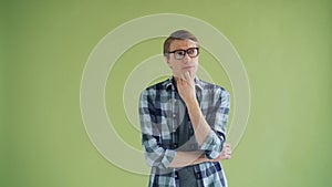 Portrait of thoughtful man in glasses looking at camera on green background