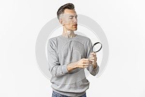 Portrait of thoughtful middle-aged man looking through magnifying glass, searching for something or reading, standing