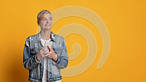 Portrait Of Thoughtful Middle Aged Woman With Smartphone Over Yellow Background