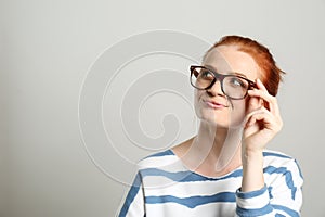 Portrait of thoughtful red haired woman with glasses on light background, space for text