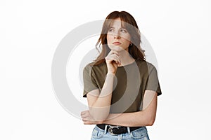 Portrait of thoughtful redhead woman looking at upper left corner, touch chin and thinking, pondering or making choice