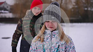 Portrait of thoughtful sad teenage girl standing in winter park as boy pulling hair running away. Offended Caucasian