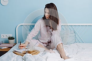 Portrait of thoughtful serious confident brunette friendly smart girl sitting on bed talking on phone, drinking coffe