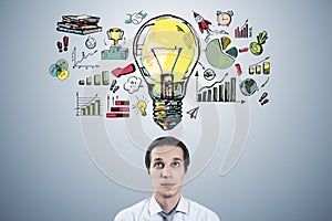 Portrait of thoughtful young businessman with creative business sketch with huge light bulb and other icons. Idea, innovation and