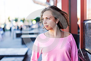 Portrait of thoughtful young Caucasian woman stands near modern building and looks away