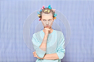 Portrait of thoughtful young woman with colorful hair curlers on head