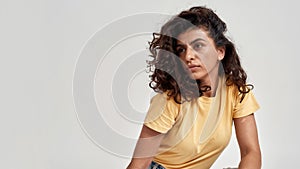 Portrait of thoughtful young woman with dark curly hair in casual wear looking aside, posing isolated over gray