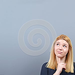 Portrait of thoughtful young woman looking at blank space above her head against gray background