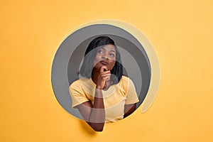 Portrait of a thoughtful young  woman looking up in a round hole circle in orange background. Copy space