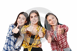 Portrait of three beautiful young happy females smiling joyfully showing thumbs up isolated on white