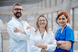 Portrait of three doctors, looking at camera, smiling. Healthcare team in medical uniforms in hospital.