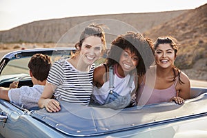 Portrait Of Three Female Friends Enjoying Road Trip In Open Top Classic Car