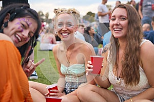 Portrait Of Three Female Friends Wearing Glitter Having Fun At Summer Music Festival Holding Drinks