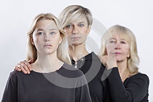 Portrait of three generations of blonde women in a family. Serious mother, grandmother and granddaughter in black sweaters stand