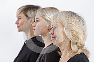 Portrait of three generations of blonde women in a family. Serious mother, grandmother and granddaughter in black sweaters stand