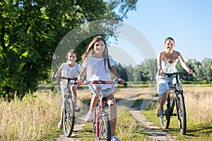 Portrait of three happy girls riding bicycles in field at sunny day