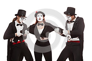 Portrait of three mime artists performing,  on white background. Two men pull the girl to sides, can not divide