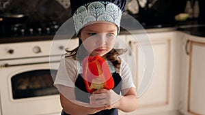 Portrait of a three-year-old girl in a apron in the kitchen with red pepper.