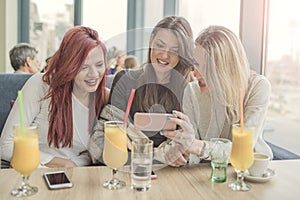 Portrait of three young beautiful women using mobile phone at co