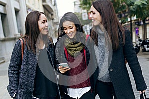 Portrait of three young beautiful women using mobile phone.