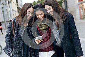 Portrait of three young beautiful women using mobile phone.