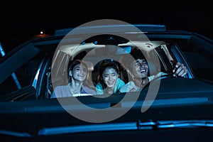 Portrait of three young friends looking emotional, laughing while sitting together in the car and watching a movie in a