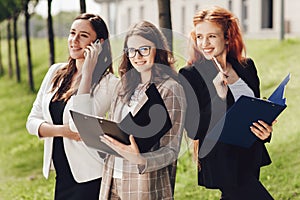 Portrait of three young successful businesswomen standing outdoors near office building on a sunny day.