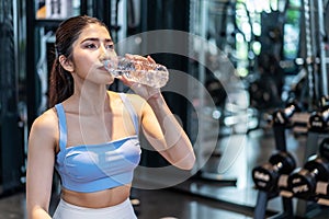 Portrait of tired asian woman in sportswear drinking water from bottle in gym. Female athlete replenishing water balance