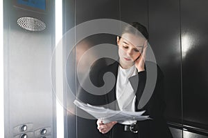 Portrait of tired bothered businesswoman reading papers in the elevator. Close up photo of concerned female employee in the lift