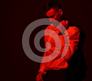 Portrait of tired businessman in official suit holding his jacket over shoulder, looking down. Red light filter, gel