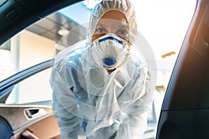 Portrait of tired exhausted female doctor, scientist or nurse wearing face mask and biological hazmat protective suit open car