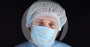 Portrait. Tired eyes of the surgeon look at the camera on a black isolated background. A doctor in a surgical uniform is