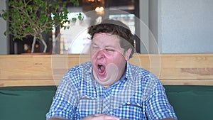 Portrait of tired fat man who yawns in cafe or restaurant