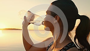 Portrait of a tired girl after a workout drinking water from a bottle at sunset