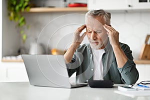 Portrait Of Tired Senior Man Suffering Headache While Working On Laptop At Home