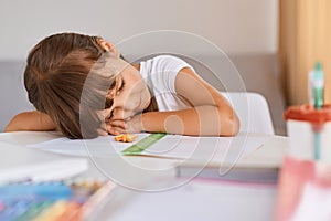 Portrait of tired sleepy child girl with dark hair doing homework being tired of long hours learning, sleeping on table on her