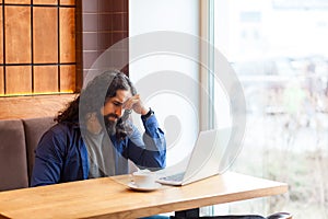 Portrait of tired thoughtful handsome young adult man freelancer in casual style sitting in cafe with laptop, trying to