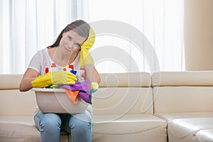 Portrait of tired woman with basket of cleaning supplies sitting on sofa at home