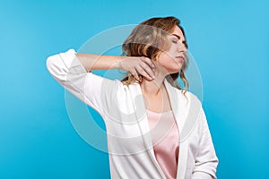 Portrait of tired woman suffering neck ache, standing with closed eyes and massaging neck to relieve pain. blue background