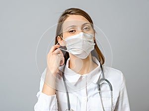 Portrait of tired young doctor taking off medical face mask