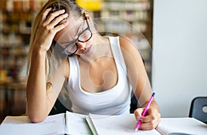 Portrait of tired young female studying in a library. Education study teenager concept