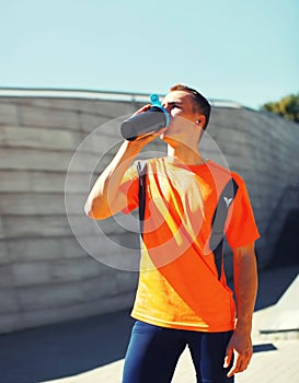 Portrait of tired young runner man drinking from bottle the water or protein shake, male sportsman resting after hard training in