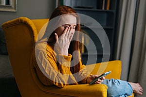 Portrait of tired young woman having blurry vision is rubbing and squinting eyes while typing using smartphone.