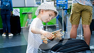 Portrait of little toddler boy playing with wooden airplane while waiting for flight in airport