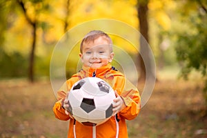 Portrait of toddler boy with soccer ball in autumn park. Healthy childhood, sports and outdoor activities concept