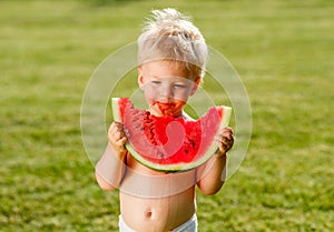 One year old baby boy eating watermelon in the garden