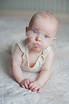 Portrait of a toddler close-up, girl blowing lips. A cute baby lying on the bed and sends an air kiss