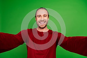 Portrait of toothy beaming handsome guy with long hairstyle wear red sweatshirt smile on selfie isolated on green color