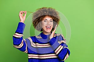 Portrait of toothy beaming pleasant girl with perming coiffure dressed knit pullover holding curl isolated on green photo